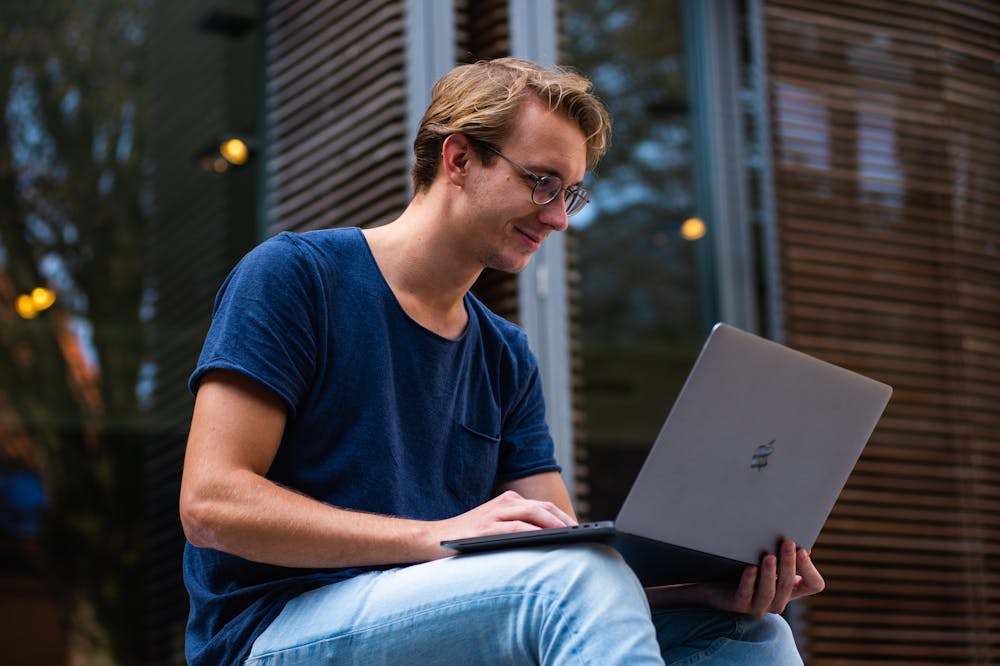 Homem sorridente, sentado ao ar livre, usando blusa azul enquanto segura um notebook. Ilustração do texto sobre como escolher uma franquia para investir.
