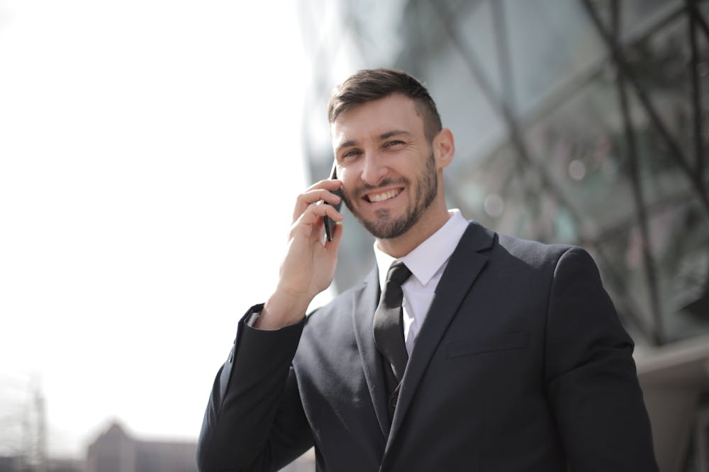 Homem sorridente usando terno na cor preta, enquanto usa o celular. Ilustração do texto sobre afinal o que é uma franquia.