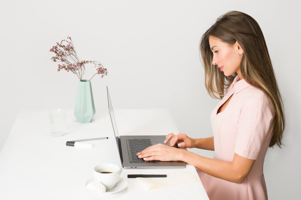 Mulher sorridente, usando vestido cor de rosa claro, enquanto usa o notebook. Ilustração do texto sobre planejamento financeiro.