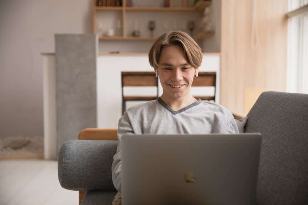 Homem sorridente, usando blusa cinza, enquanto trabalha no notebook. Ilustração do texto sobre tendências para empreender.