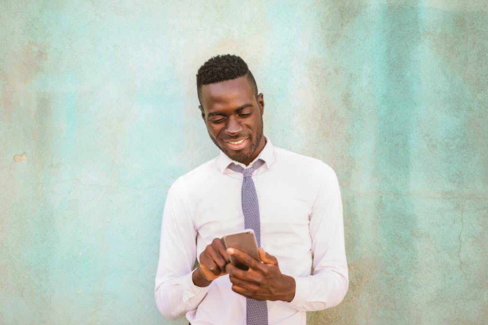 Homem sorridente, usando gravata azul e blusa social manga longa, observando o celular. Ilustração do texto sobre como funciona a franquia.