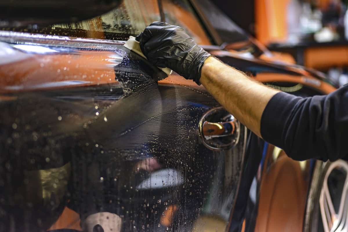 Carro preto sendo encerado por mão com luva. Ilustração do texto sobre o Acqua On.
