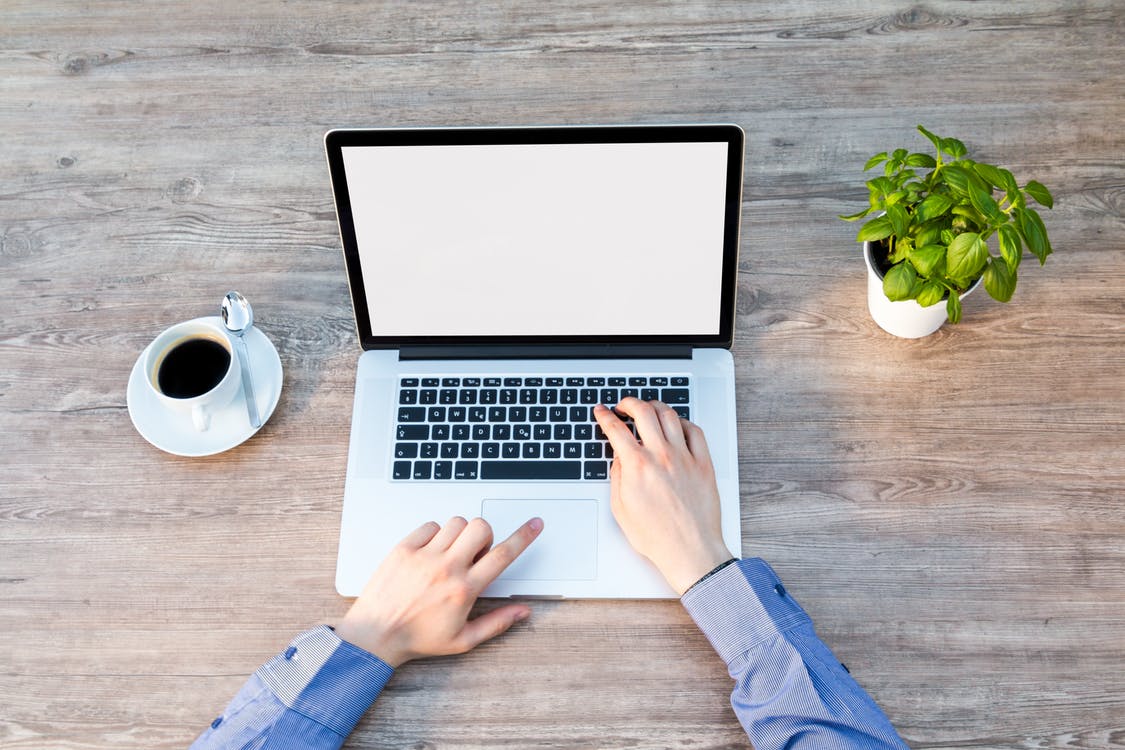 Homem mexendo no computador em uma mesa com xícara de café ao lado. 