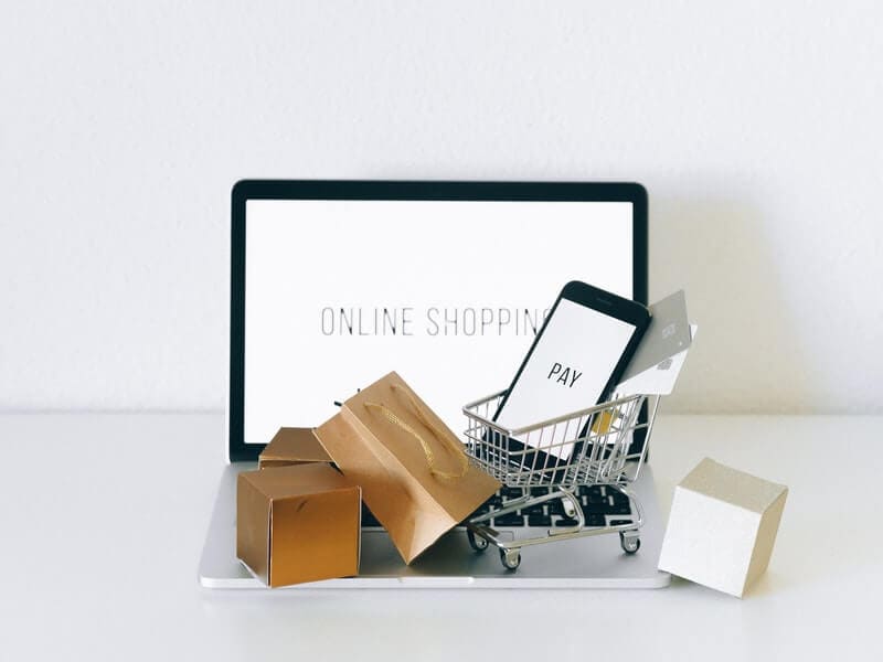 Franquias baratas online 2026 - guia rápido sobre o sistema Pequeno carrinho de compras em cima de computador ao lado de pacotes miniatura. Ilustração do texto sobre franquia de vendas on-line.