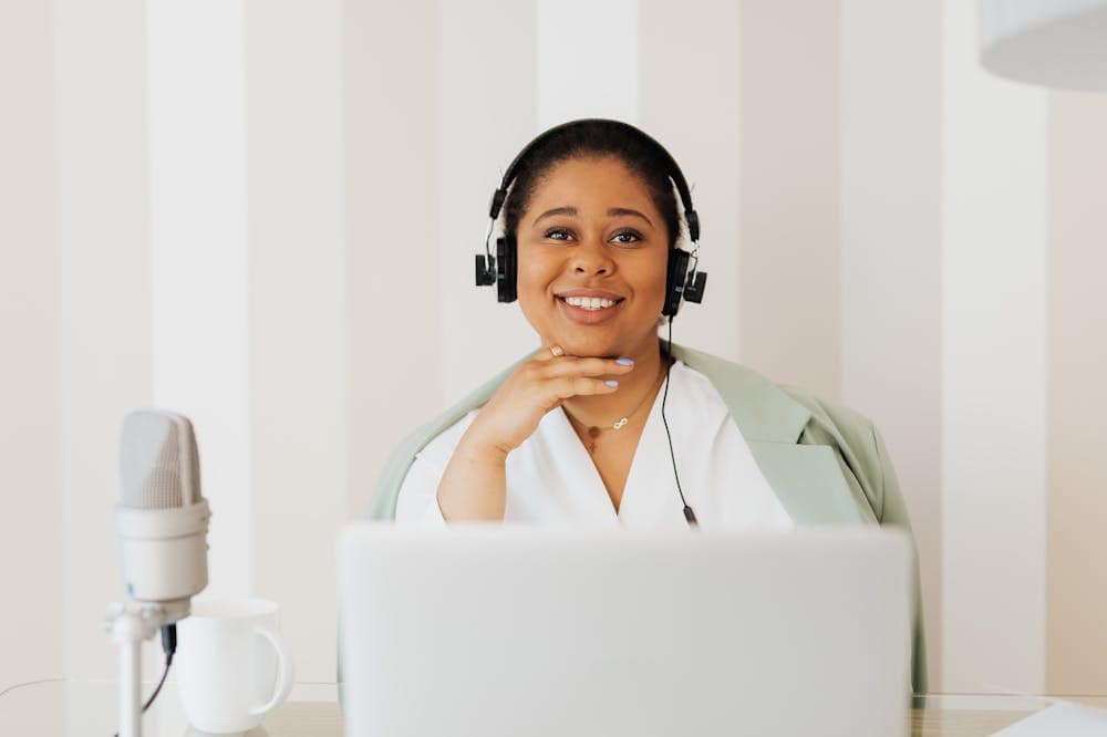 Mulher sorridente, usando blusa branca, enquanto trabalha em frente ao computador com headset. Ilustração do texto sobre processos operacionais da sua empresa.