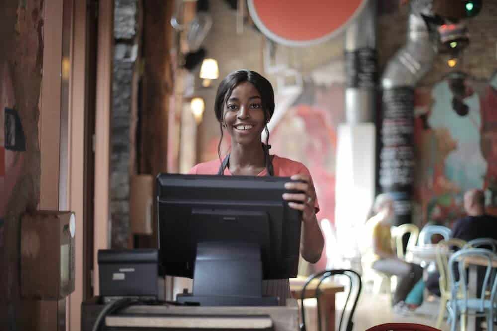 Mulher sorridente usando blusa vermelha, com as mãos sobre monitor de computador. Ilustração do texto sobre franquias que exploram o digital.