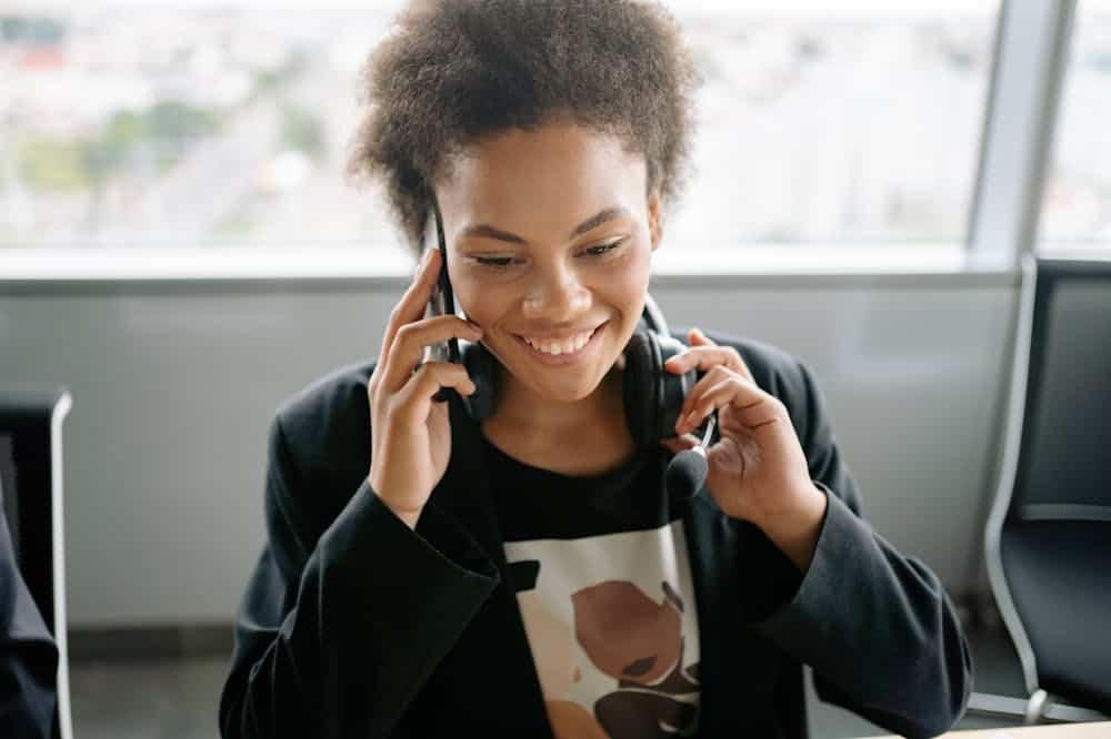 Mulher sorridente, usando blazer preto, ao telefone. Ilustração do texto sobre abrir uma empresa.