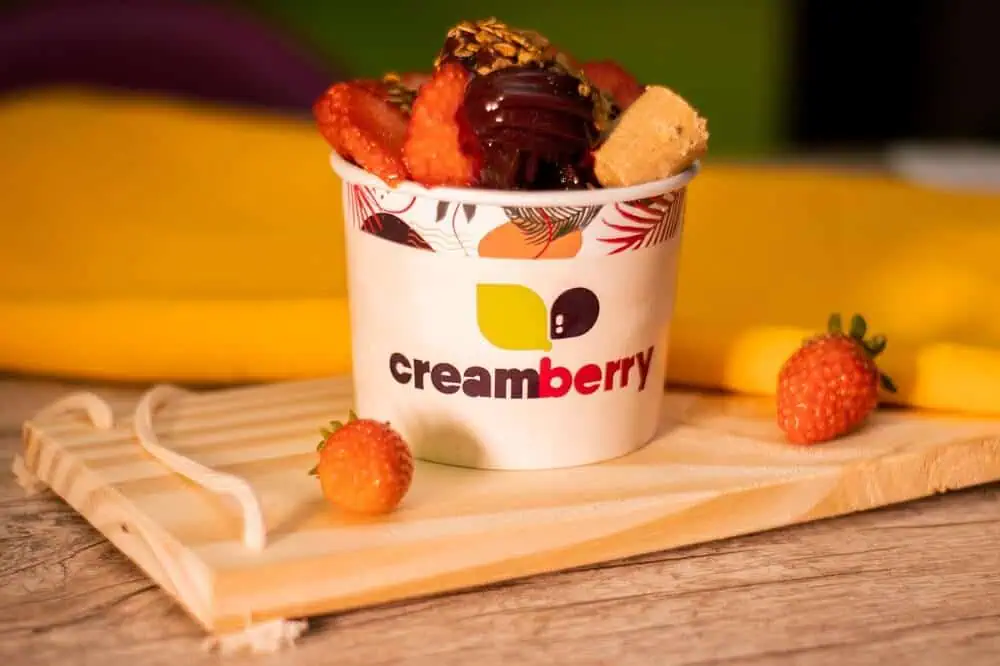 A imagem traz um pote de açaí com morangos, granola e paçoca em cima de uma bandeja de madeira. Imagem ilustrativa do texto: franquia de acai self service.