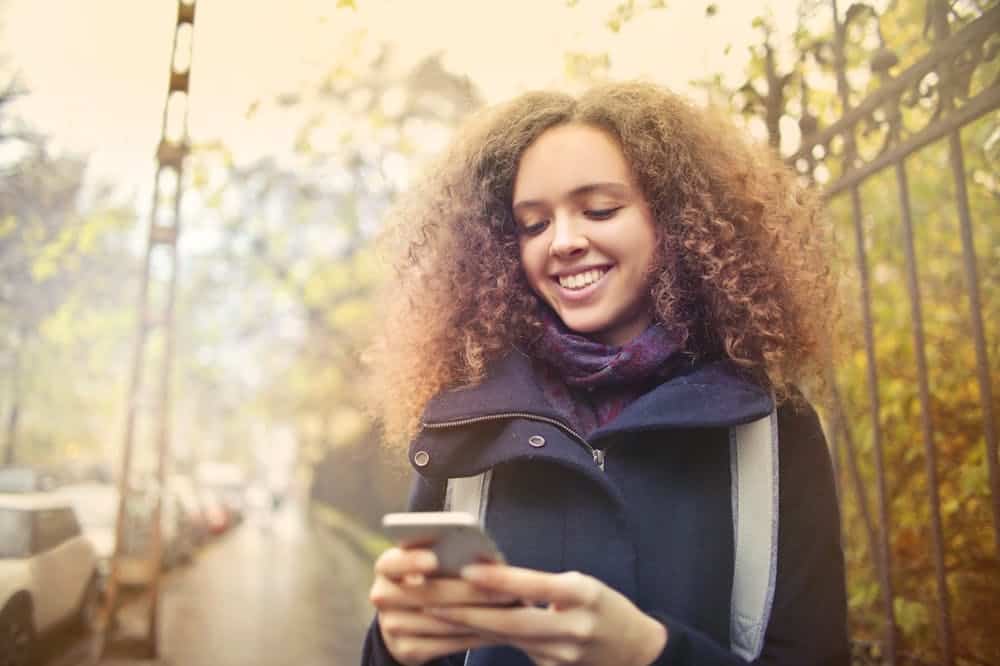 Mulher sorridente, usando blusa na cor cinza, olhando para o celular. Ilustração do texto sobre franquias até 150 mil.