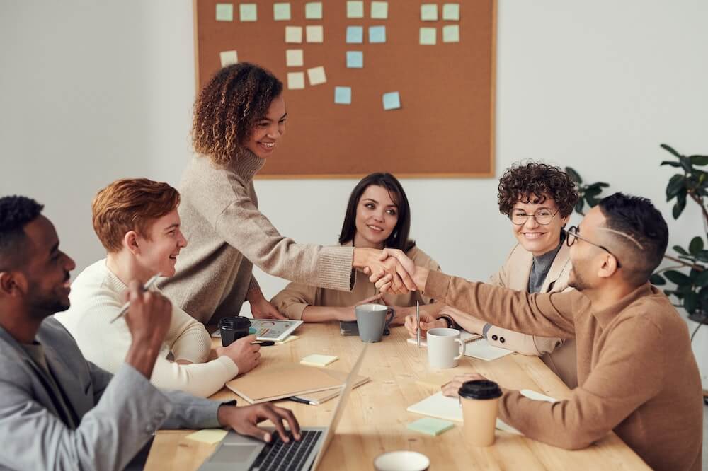 Pessoas sorridentes reunidas em torno de uma mesa marrom de uma empresa. Ilustração do texto sobre porque escolher uma franquia.