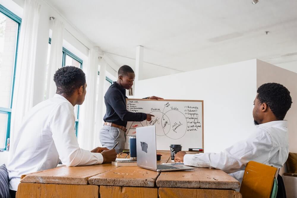 Homens reunidos analisando dados em quadro branco. Ilustração do texto sobre segmentos de franquias com baixo investimento.