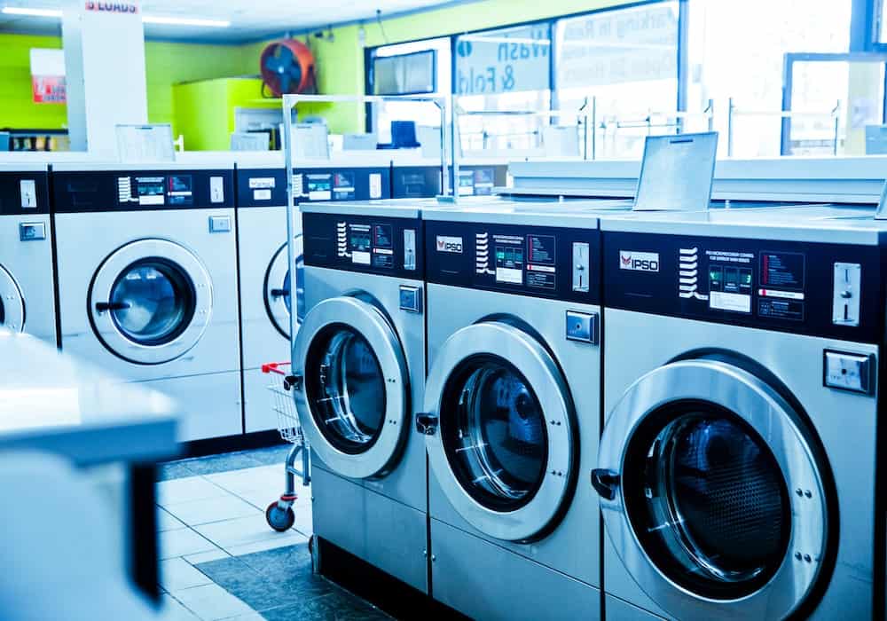 7 Nichos promissores para você investir ainda este ano Imagem do interior de uma lavanderia com máquinas de lavar uma ao lado da outra. Imagem ilustrativa texto franquia de lavanderia.