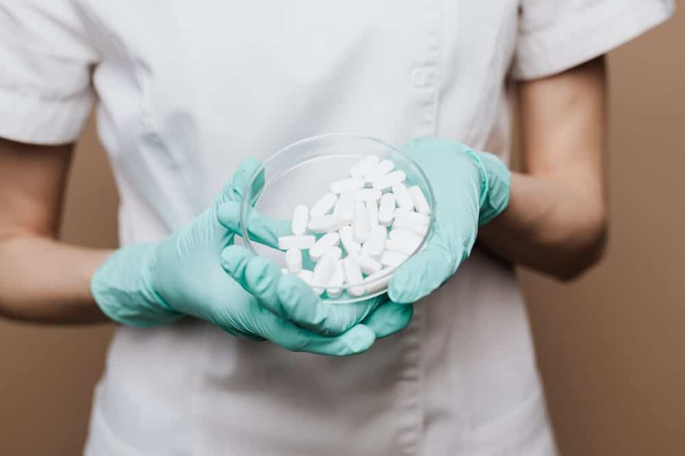 Pessoa, usando luvas, segurando recipiente com comprimidos brancos. Ilustração do texto sobre franquia compre certo.