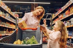 Mulher sorridente, usando blusa cor de rosa, olhando para a filha, enquanto conduz um carrinho de supermercado. Ilustração do texto sobre franquia de conveniência.