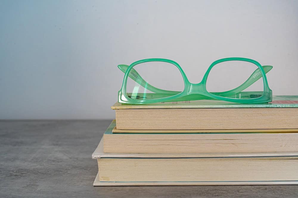 Um óculos com armação verde sobre uma pilha com três livros. Imagem ilustrativa do texto franquia de ótica.