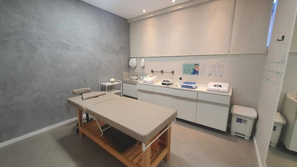 Sala de tratamento estético com uma maca e um balcão e armários na cor branca. Imagem ilustrativa do texto franquia Majô.