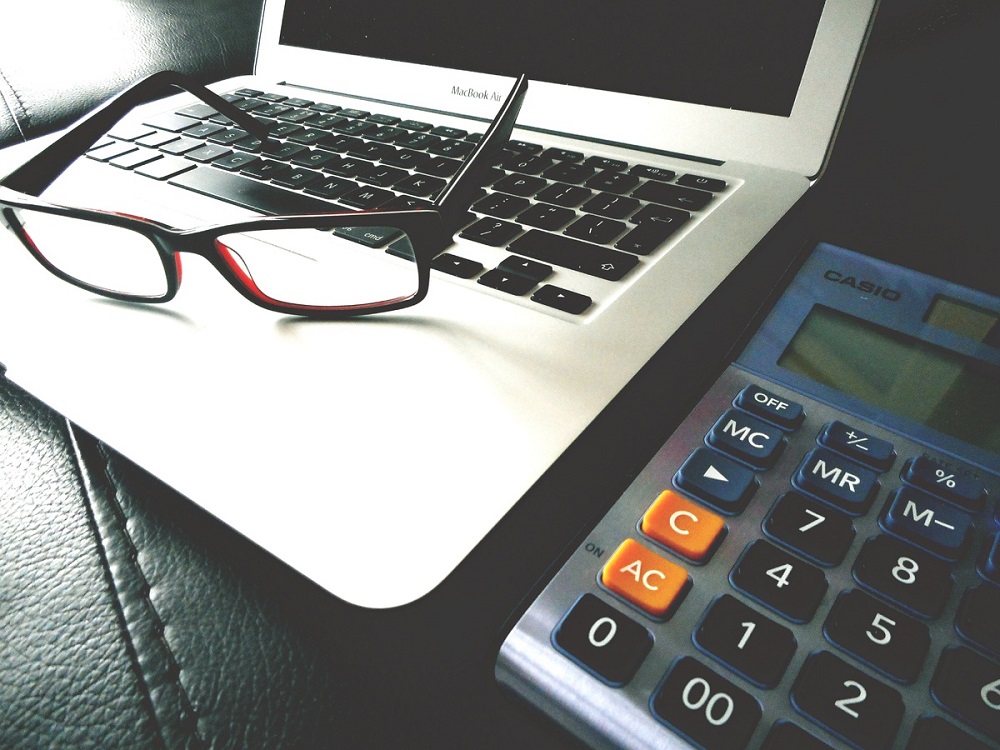 Teclado de notebook cor preta com um óculos por cima e uma calculadora ao lado. Imagem ilustrativa do texto franquias baratas e rentáveis para 2023.