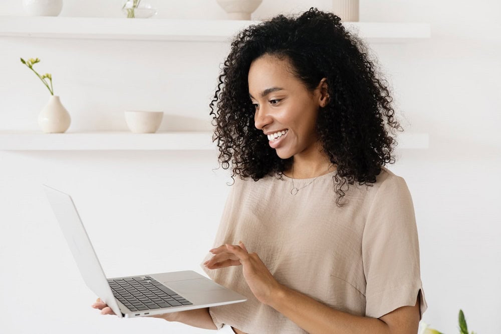 Mulher sorrindo, usando blusa bege, com um computador na mão mexendo no teclado. Imagem ilustrativa do texto sobre franquias que valem a pena.