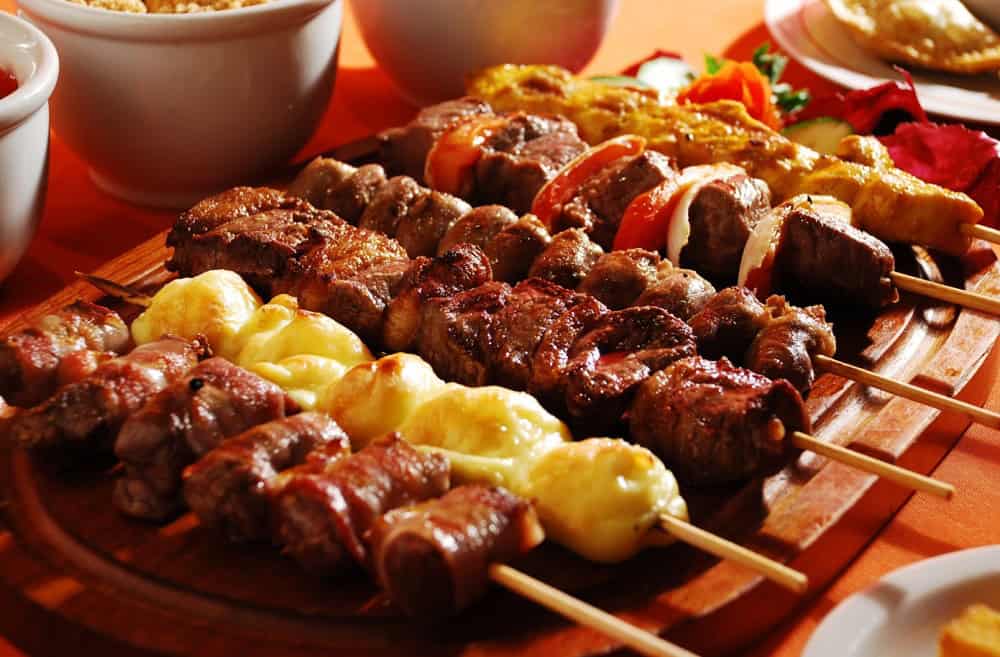 Espetinhos de carne e queijo em tábua de madeira marrom. Ilustração do texto sobre franquia de espetinhos.