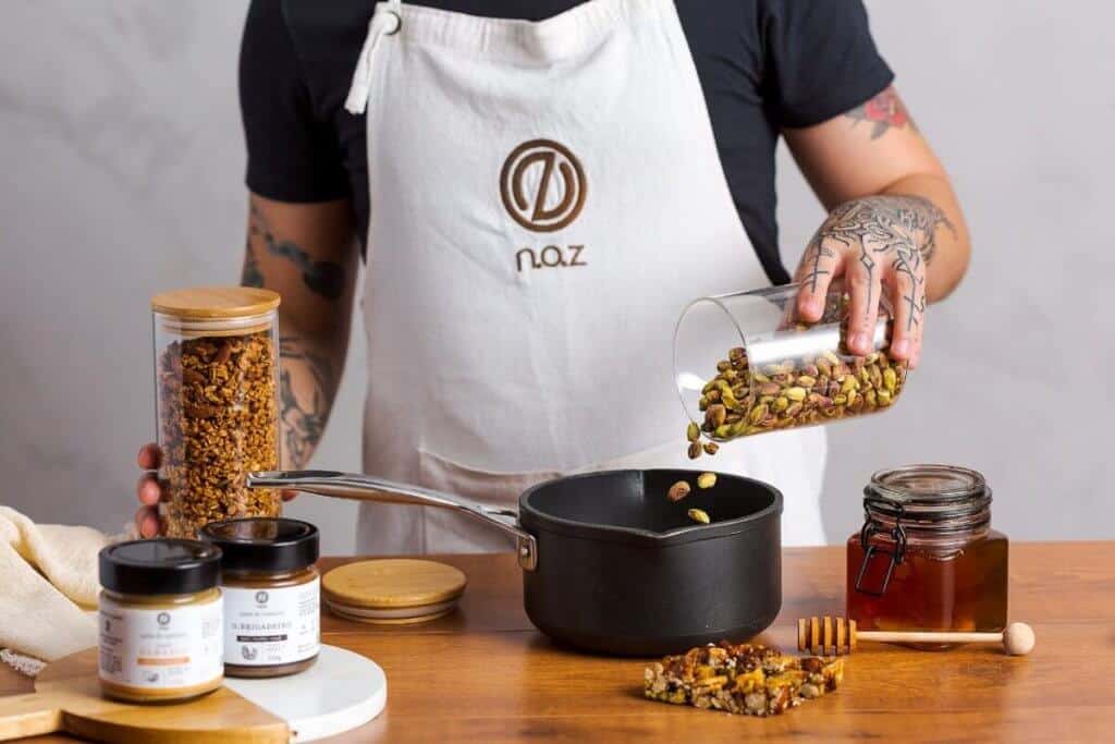 Homem usando avental branco misturando castanhas em um panela preta. Ilustração do texto sobre franquia Noz.