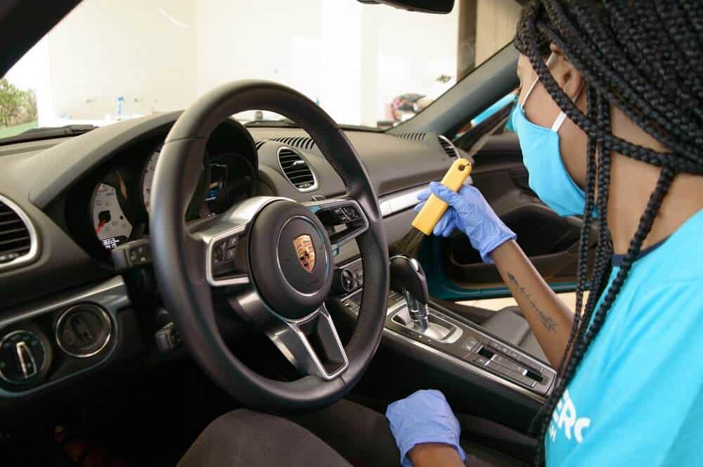 Mulher usando máscara e luvas na cor azul higienizando um carro. Ilustração do texto sobre franquias no setor automotivo.