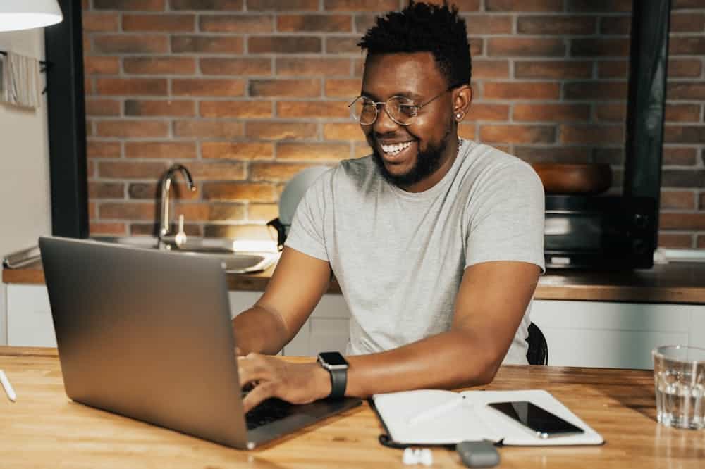 Franquias baratas online 2026 - guia rápido sobre o sistema Homem sorridente trabalha em notebook cinza. Ilustração do texto sobre como abrir um ecommerce.