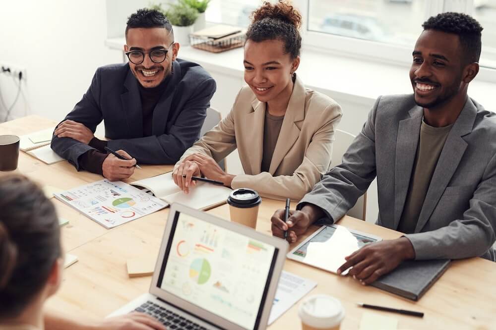Grupo de empreendedores sorrindo, reunidos em volta de uma mesa marrom claro. Ilustração do texto sobre empreendedor franqueado.