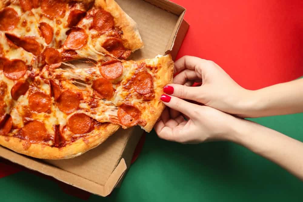 Mãos femininas, usando esmalte vermelho, pegando pedaço de pizza. Ilustração do texto sobre como abrir uma pizzaria delivery 2.
