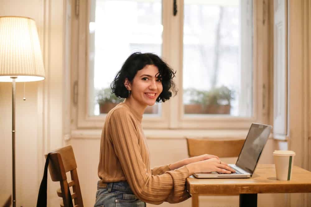 Mulher sorridente, trabalhando em seu computador cinza. Ilustração do texto sobre curso de franquias.