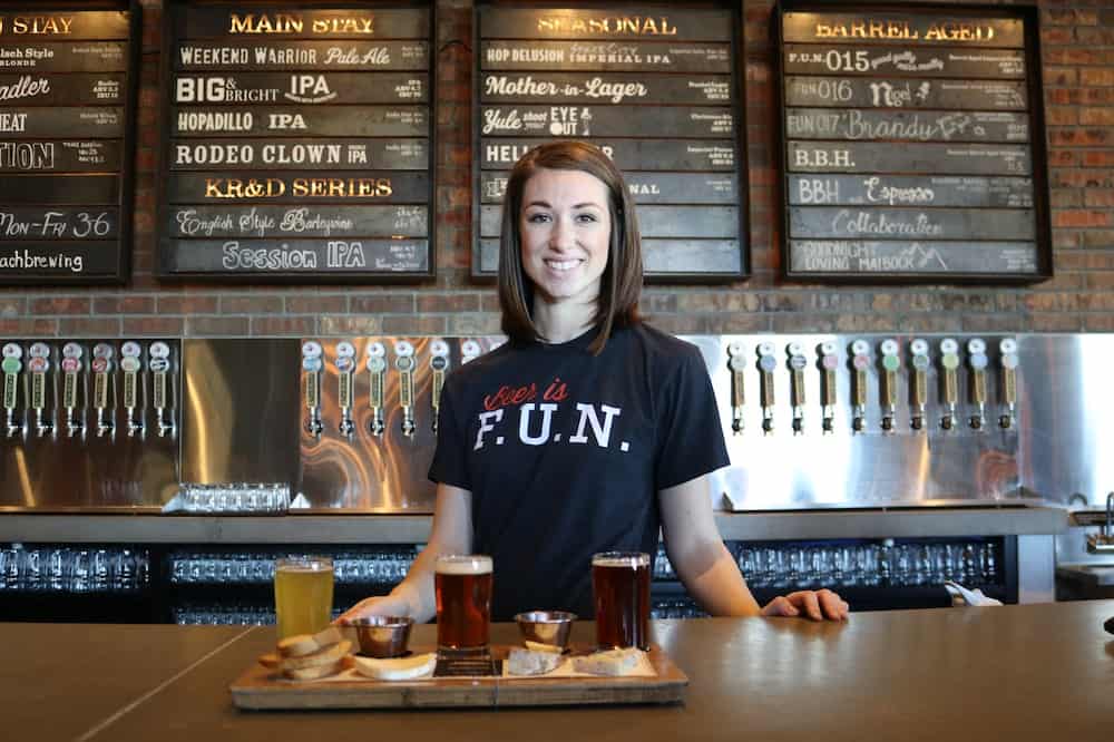 Mulher sorridente usando camisa preta atrás de um balcão de bar. Ilustração do texto sobre franquias de bares e restaurantes.
