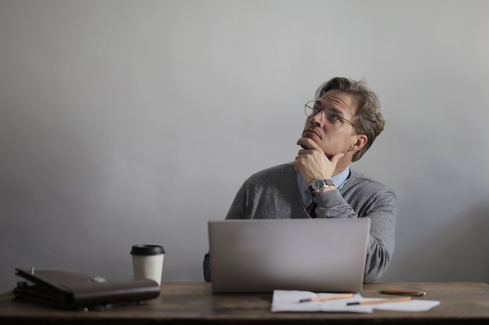 Homem pensativo em frente a um notebook na cor cinza. Ilustração do texto sobre franquia 40 mil.