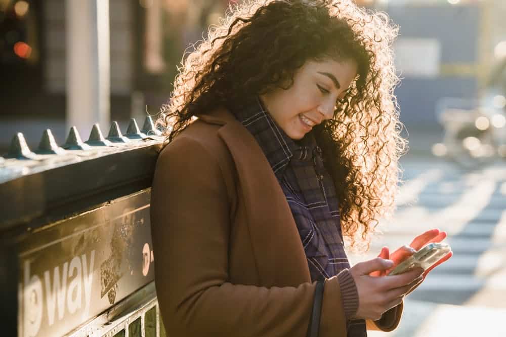 Mulher sorridente, usando blazer marrom, enquanto observa o celular. Ilustração do texto sobre negócios e oportunidades.