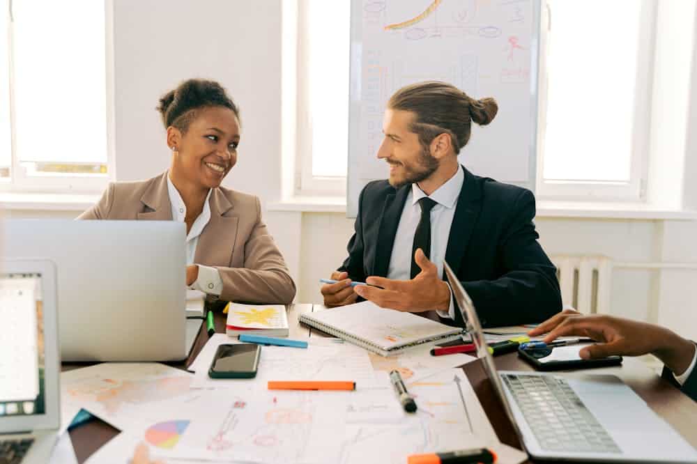 Homem e mulher sorridentes, sentados lado a lado em mesa de escritório com computador cinza. Ilustração do texto sobre contrato de franquia de corretora de seguros.