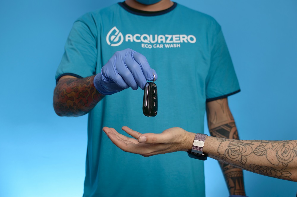 Homem usando blusa azul da Acquazero, entregando a chave do carro para alguém. Ilustração do texto sobre franquia de estética automotiva.