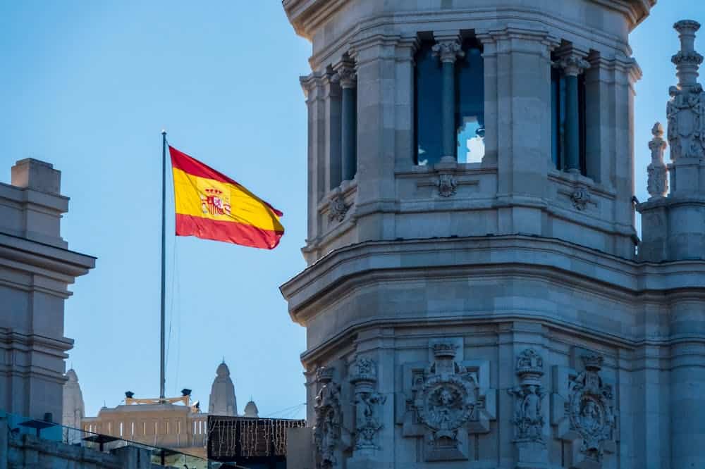 Bandeira amarela e vermelha da Espanha, se destacando com o céu azul ao fundo. Ilustração do texto sobre abrir franquia Espanha.