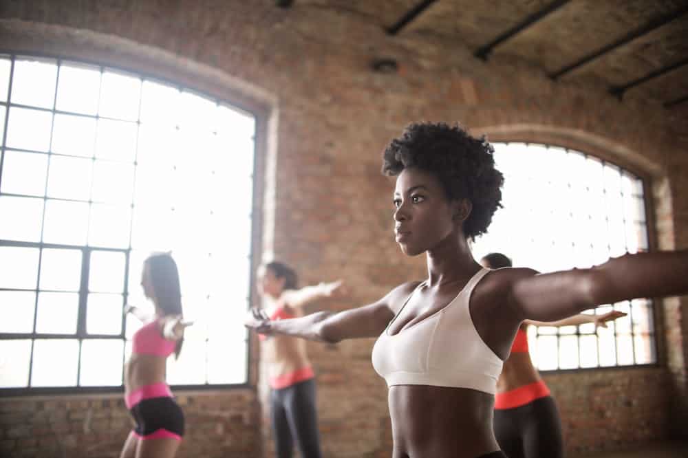 Mulher atenta, usando top branco, se exercitando em uma academia. Ilustração do texto sobre franquias fitness.