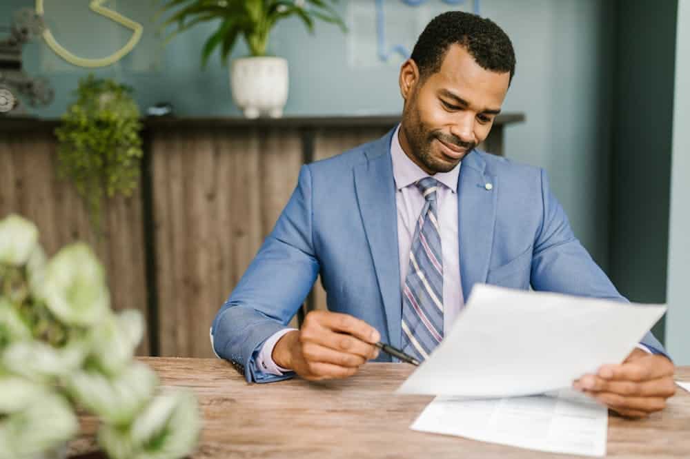 Homem sorridente, usando terno azul claro, observando papéis. Ilustração do texto sobre franquias mais seguras para se investir.