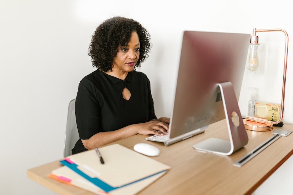 Mulher atenta, usando blusa na cor preta, trabalhando em frente a um computador com monitor cinza. Ilustração do texto sobre franquias para empreender.