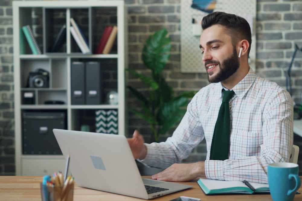 Microfranquias online: Opções para você trabalhar em casa Homem sorridente, usando gravata preta, usando o notebook. Ilustração do texto sobre microfranquias.