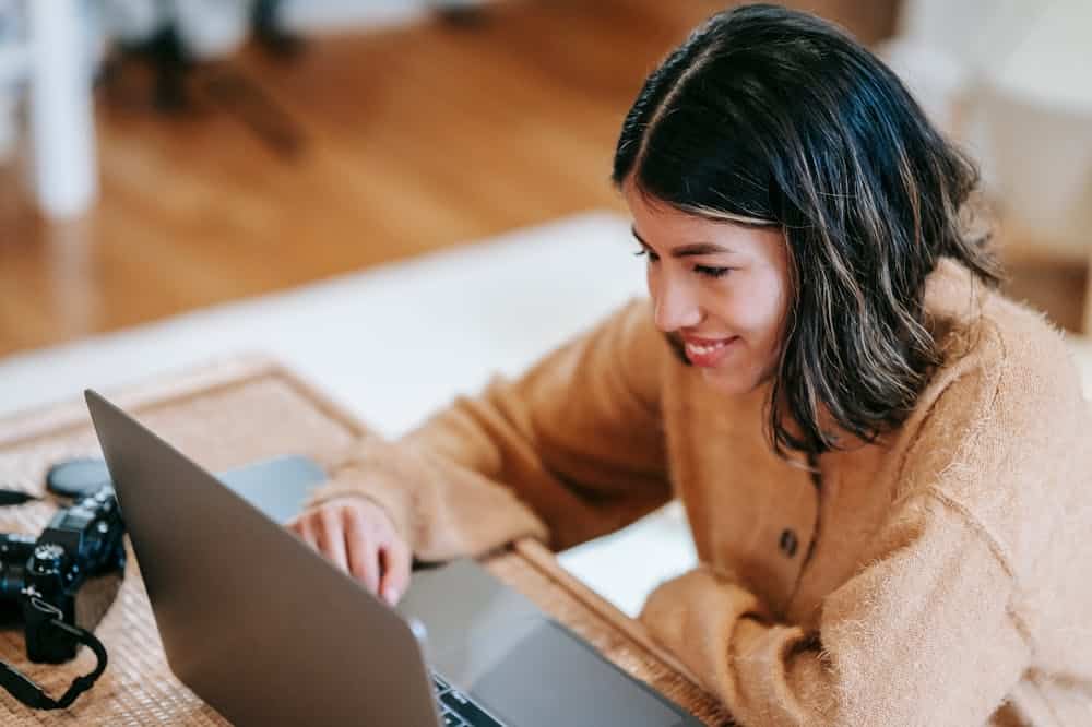 Mulher sorridente, usando blusa na cor bege, trabalhando em frente ao computador. Ilustração do texto sobre mini franquias.