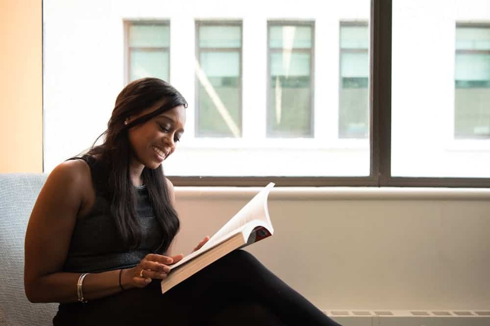 Mulher sorridente, usando roupa preta, enquanto lê um livro. Ilustração do texto sobre história do franchising.