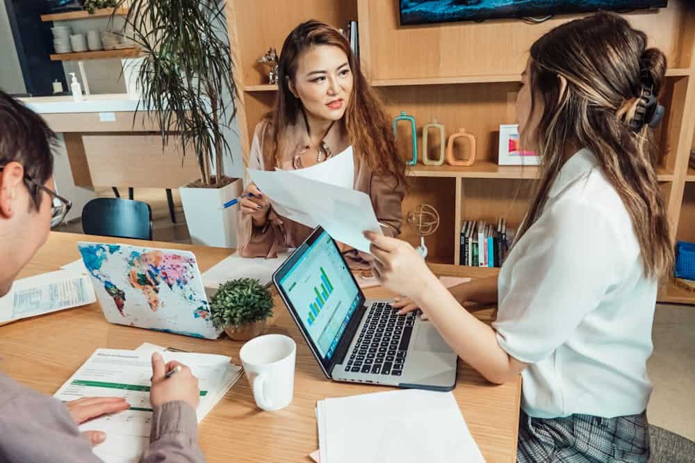 Franquia como funciona? Modelo de negócio cresce 10% ao ano Mulheres conversando, sentadas em torno de mesa marrom. Ilustração do texto sobre franquia de baixo investimento e alta rentabilidade.