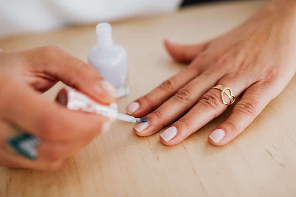Pessoa passando esmalte branco nas unhas. Ilustração do texto sobre franquia de manicure express.