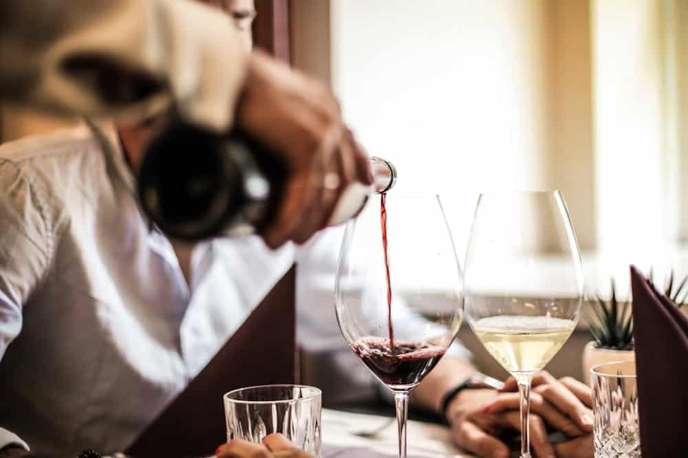 Pessoa colocando vinho tinto na cor bordo em uma taça. Ilustração do texto sobre franquia de vinhos.