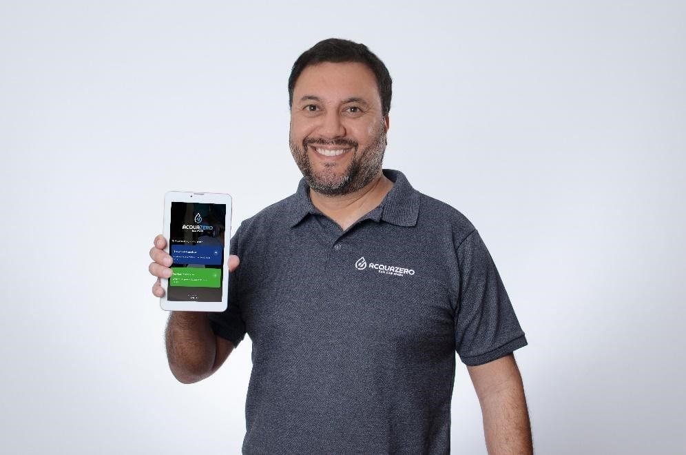 Henrique Mol, CEO da franquia Acquazero, segura na mão um tablet que tem na tela o aplicativo da Acquazero.