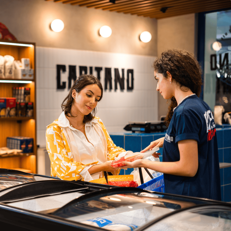 Cliente e atendente com pescada em frente à freezer Capitano.