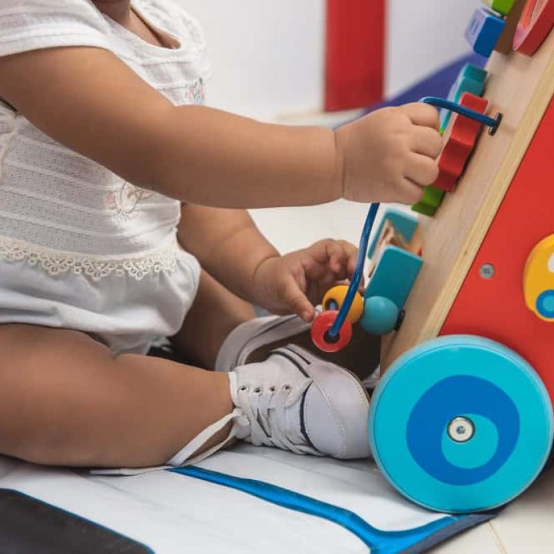 A foto mostra o tronco de uma criança sentada brincando com um item colorido.