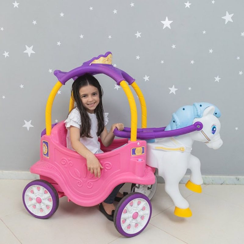 Criança menina sentada em um carrinho de unicórnio e feliz, sorrindo para a câmera.