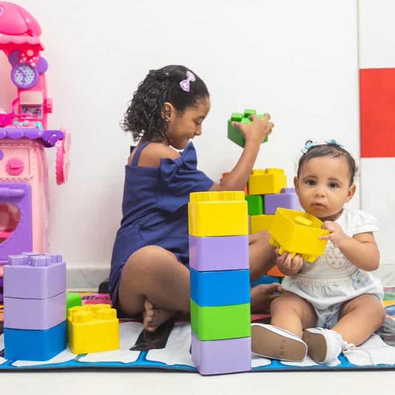 Crianças sentadas brincando com brinquedos coloridos.