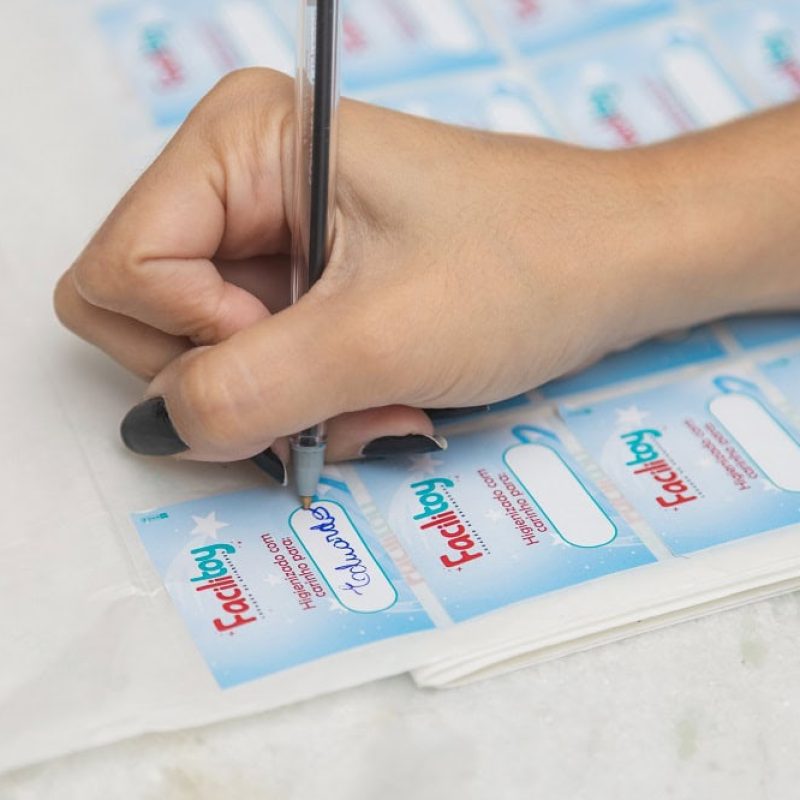 Mão de mulher escrevendo em etiquetas para brinquedos Facilitoy.